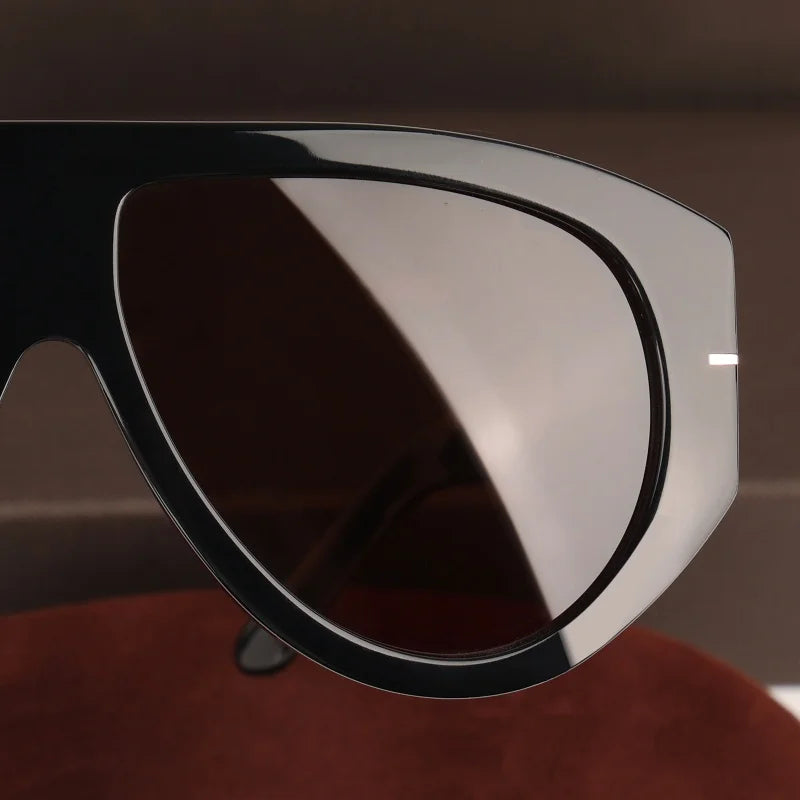 A close-up view of oversized pilot sunglasses with dark lenses and a silver frame resting on a reddish fabric.