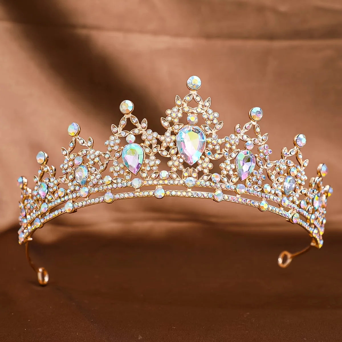 Diadema de tiara barroca de cristal brillante con piedras transparentes e iridiscentes, mostrada sobre tela marrón.