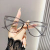 Eine Hand hält eine transparente Vintage Cat-Eye-Lesebrille mit Goldakzenten vor einem hellen Hintergrund.