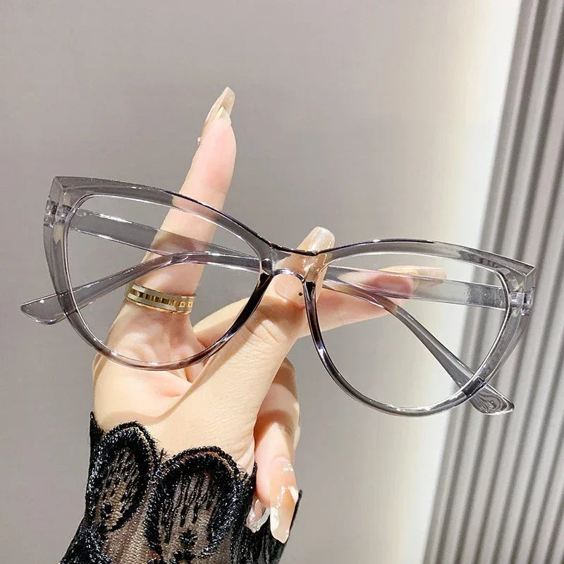 Eine Hand hält eine transparente Vintage Cat-Eye-Lesebrille mit Goldakzenten vor einem hellen Hintergrund.
