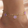 Gold jewelry featuring five-leaf clover anklets with purple stones worn on a person's ankle.