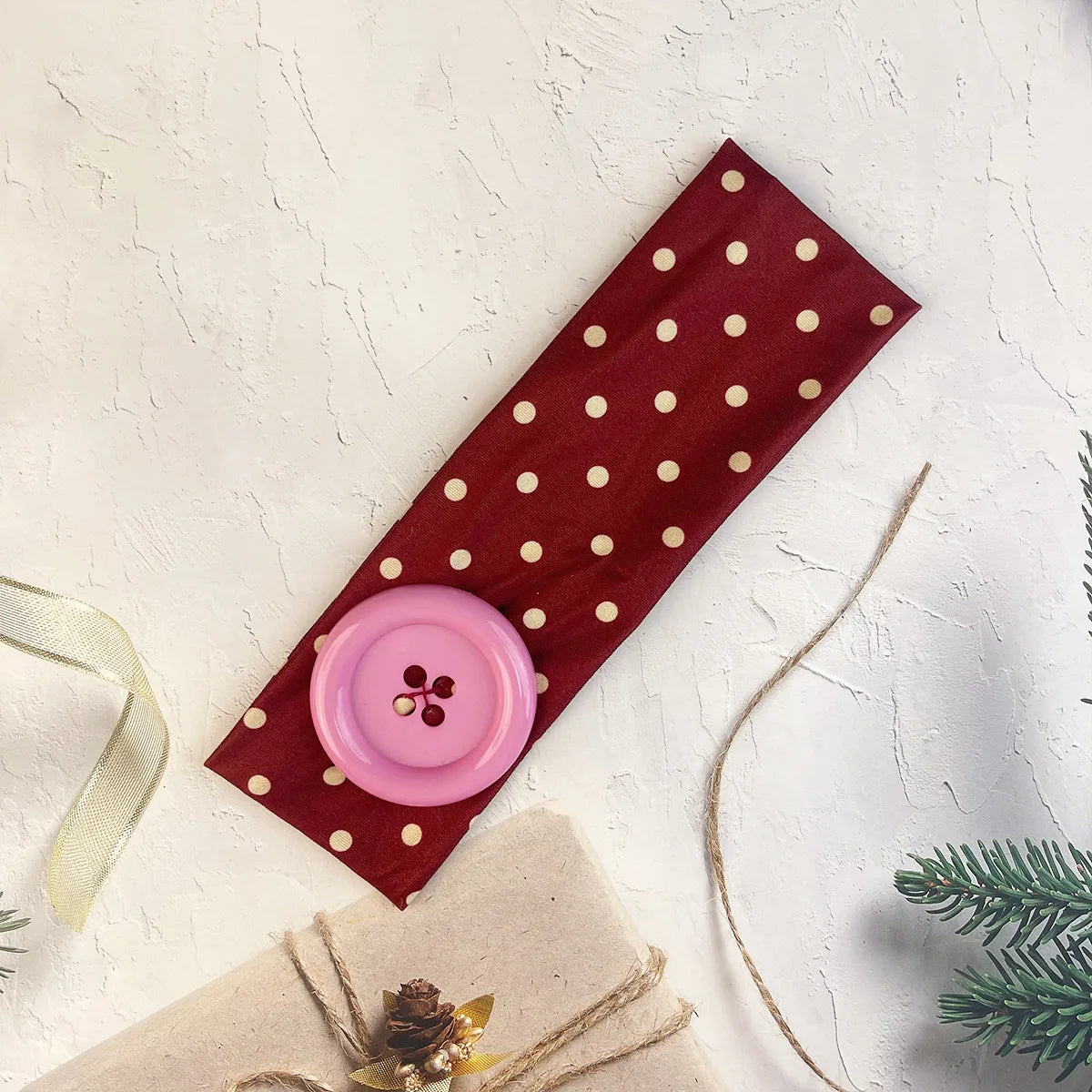 A maroon polka dot fabric headband with a pink button attached, tied with natural twine.