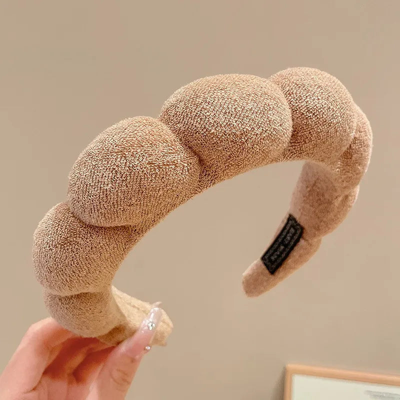 A close-up of a beige cloud sponge hair accessory headband being held by a hand.