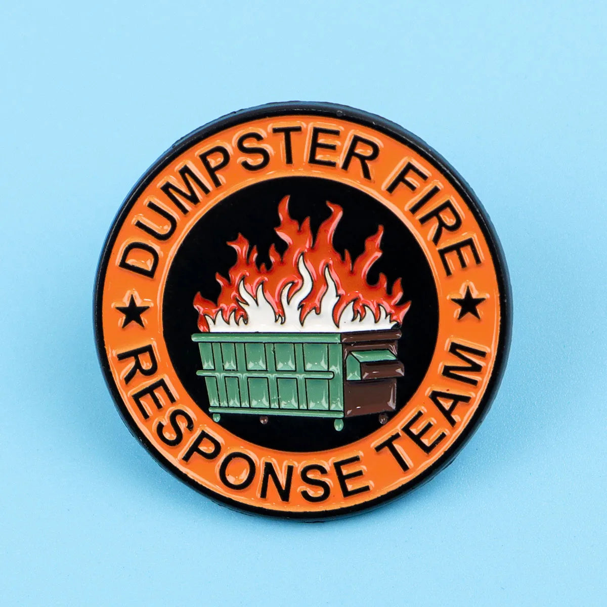 An enamel lapel pin featuring a green dumpster with flames on top, surrounded by the text DUMPSTER FIRE RESPONSE TEAM.