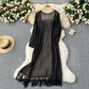 Black knitted shawl cardigan with mesh detailing draped over a white fluffy rug surrounded by white flowers