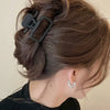 A close-up of a woman's dark brown hair styled in a half-up bun using black lightweight hair claw clips.