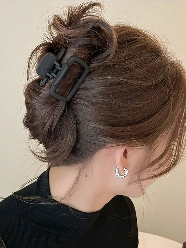 A close-up of a woman's dark brown hair styled in a half-up bun using black lightweight hair claw clips.