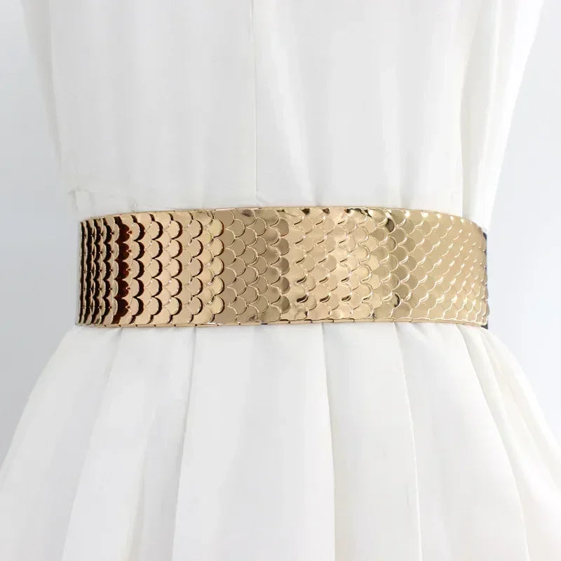 Ceinture élastique large à motif or et marron portée à la taille d'une robe blanche.
