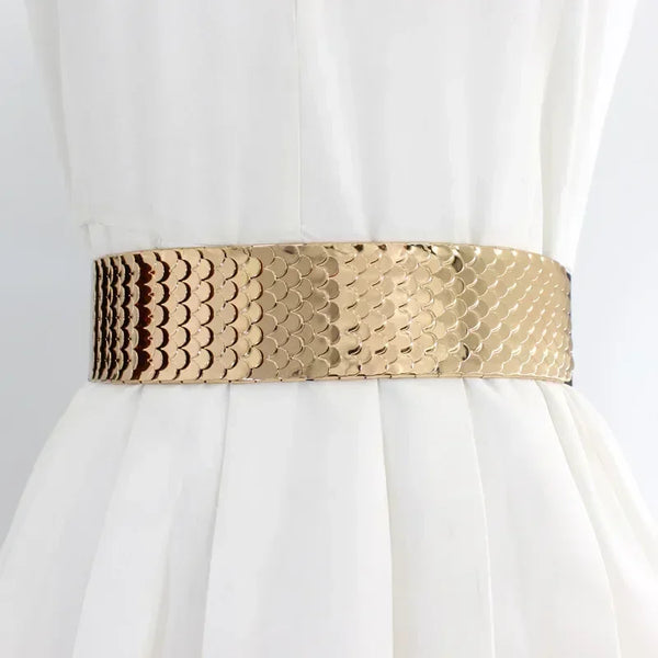 A gold and brown patterned elastic wide belt worn around the waist of a white dress.