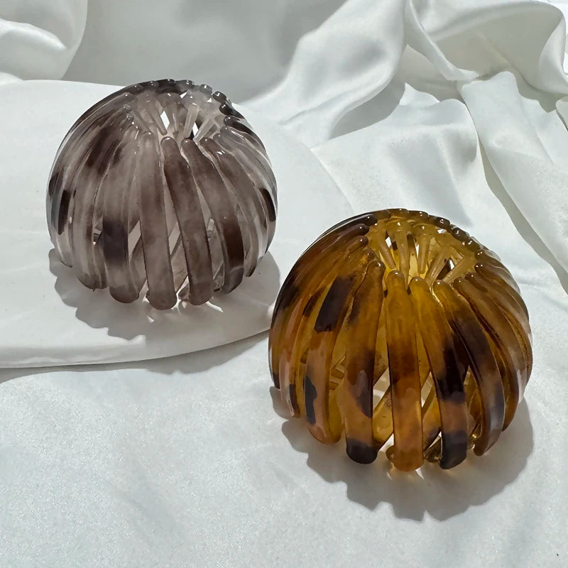 Two elegant glass horsetail hair clips, one smoky gray and one amber, displayed on white fabric.