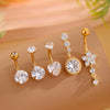 A set of five gold stainless steel dangled belly button rings with various diamond and gemstone designs displayed on a beige 
