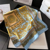 A light blue silk scarf with intricate gold baroque patterns draped on a dark surface.