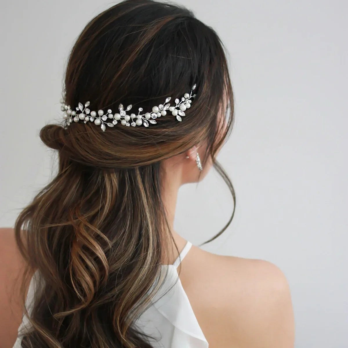 A woman with long brown hair styled in an updo wears an elegant pearl bridal headband.