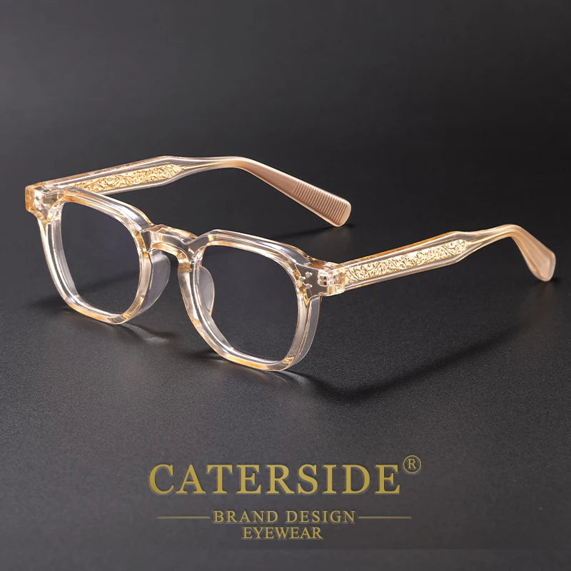 Clear acetate eyeglasses with gold detailing resting on a dark surface.
