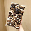 A clear plastic bag filled with brown and beige elastic hair ties for ponytails.