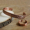 A set of vintage flower engraved copper bracelets and rings resting on a wooden surface.