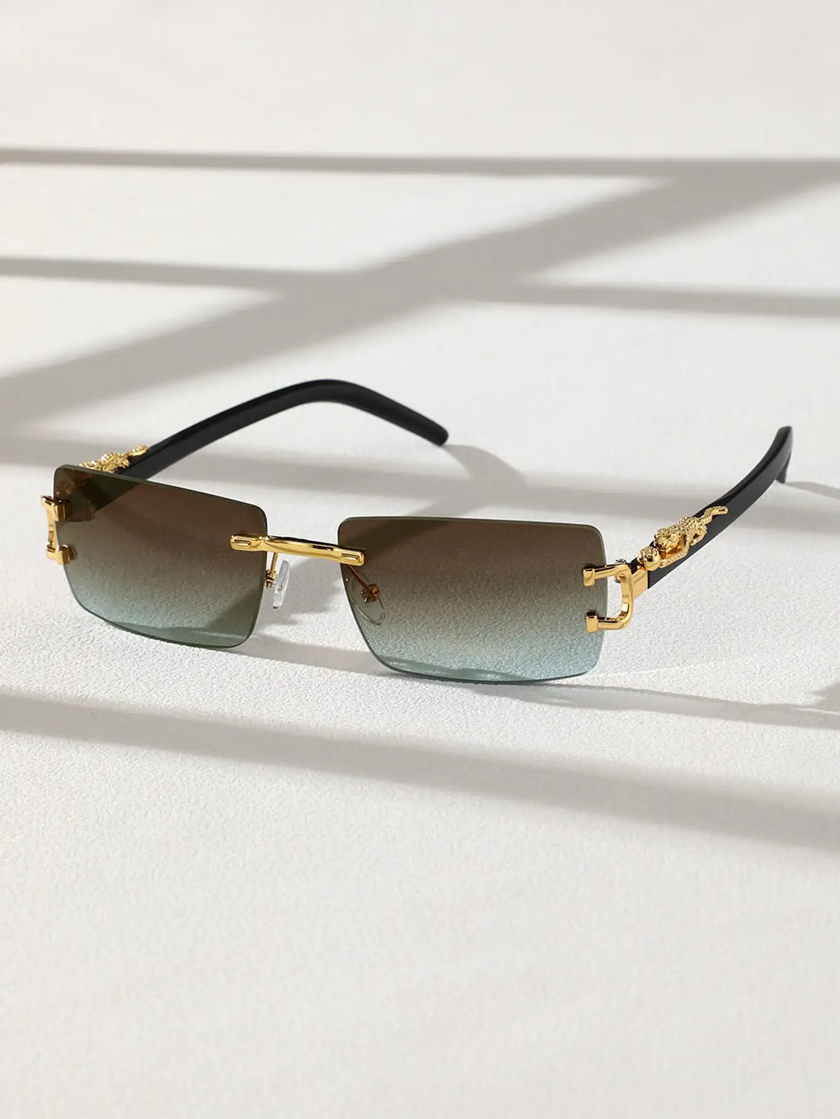 A pair of trendy frameless rectangular sunglasses with gold accents resting on a white surface.