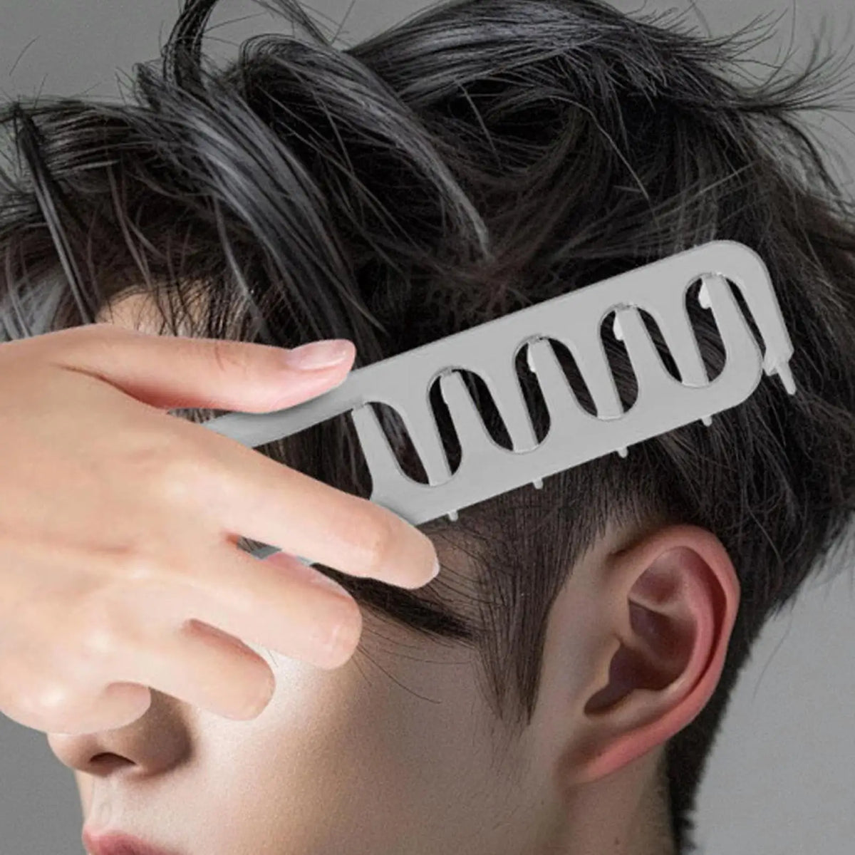 A hand is using a gray volume boosting detangling hair comb to style dark hair.