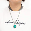 A silver necklace featuring a vibrant turquoise stone pendant worn against a white shirt.