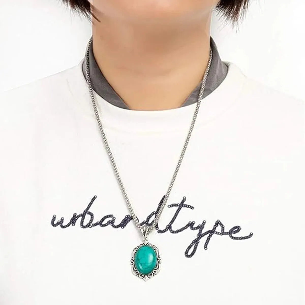 A silver necklace featuring a vibrant turquoise stone pendant worn against a white shirt.