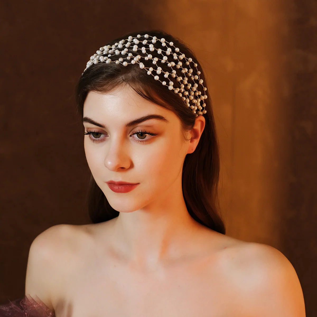 A close-up of a woman wearing an elegant pearl hair net headband against a warm brown background.