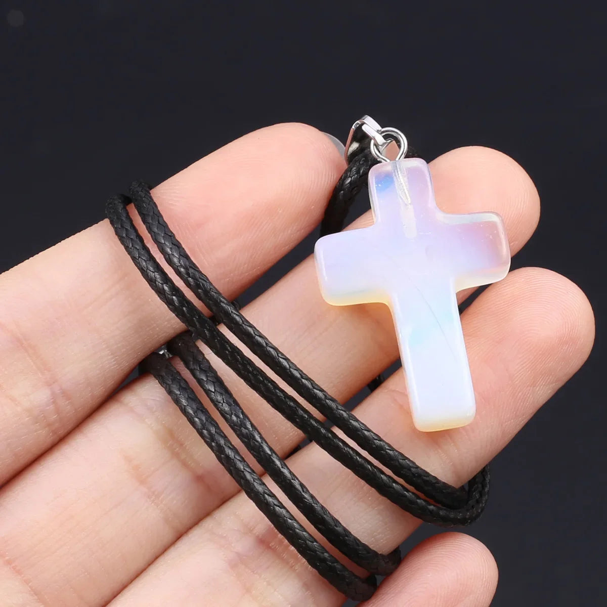 Eine Hand hält eine Tigerauge-Agat-Kreuz-Anhänger-Kette mit blassgrüner, durchscheinender Farbe.