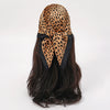 Schwarzer Satin-Schal mit Leopardenmuster, um die dunklen Haare gebunden.