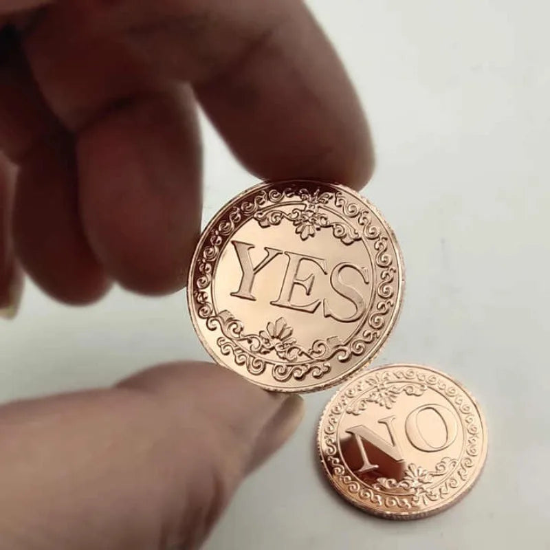 A hand holds two vintage antique bronze decision coins, one engraved with YES and the other with NO.