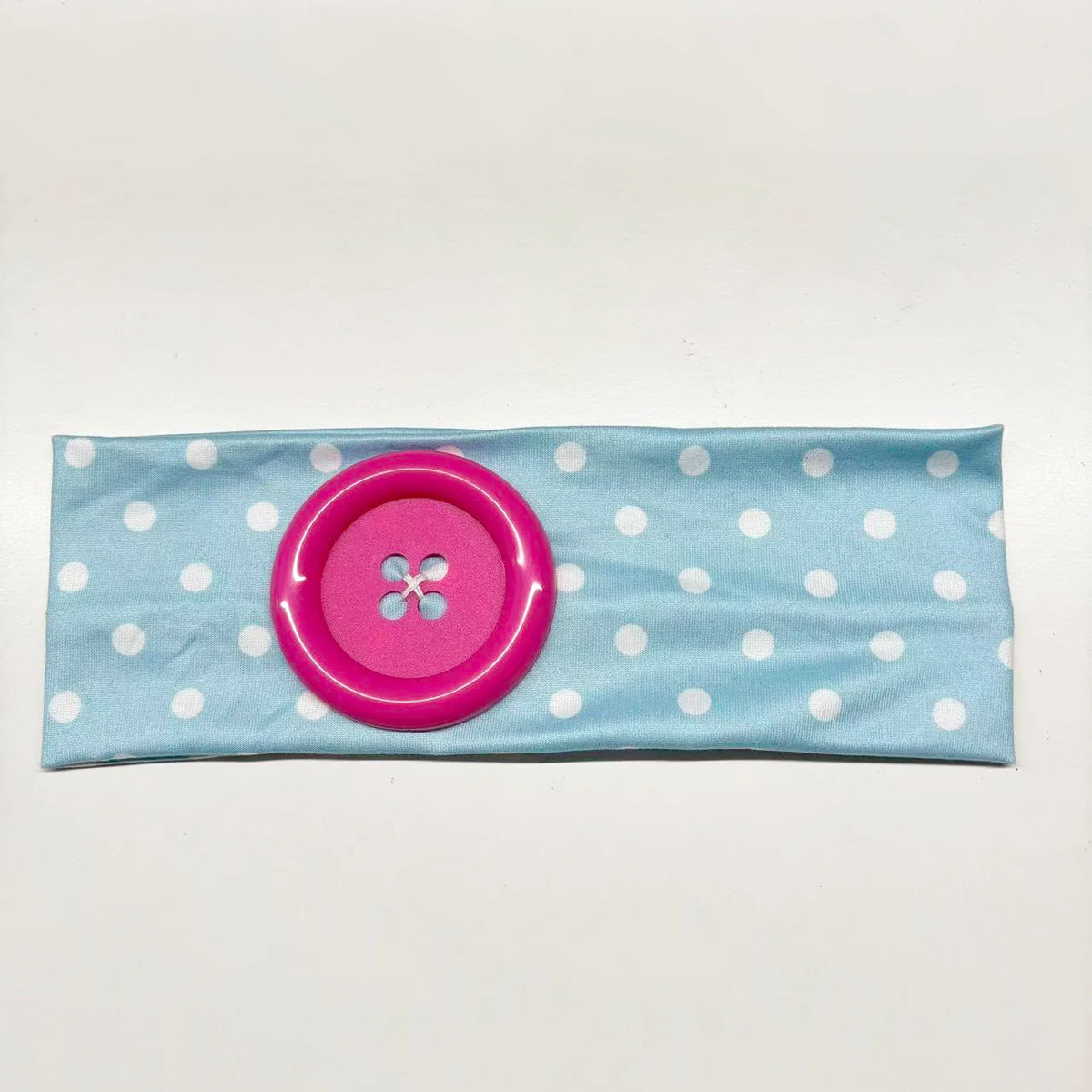 A pink polka dot fabric headband with a large pink button detail.