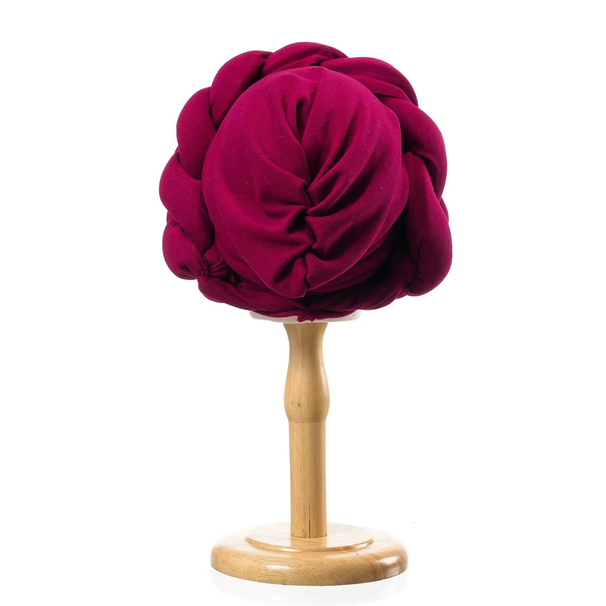 A deep magenta braided turban cap displayed on a wooden stand.