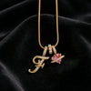 Gold alphabet pendant necklace featuring the letter F and a pink gemstone flower on a black velvet background
