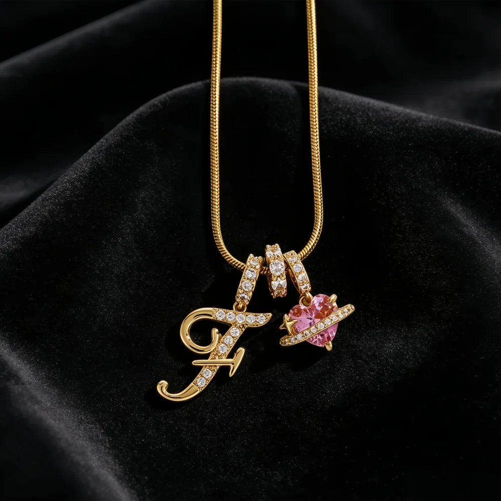 Gold alphabet pendant necklace featuring the letter F and a pink gemstone flower on a black velvet background
