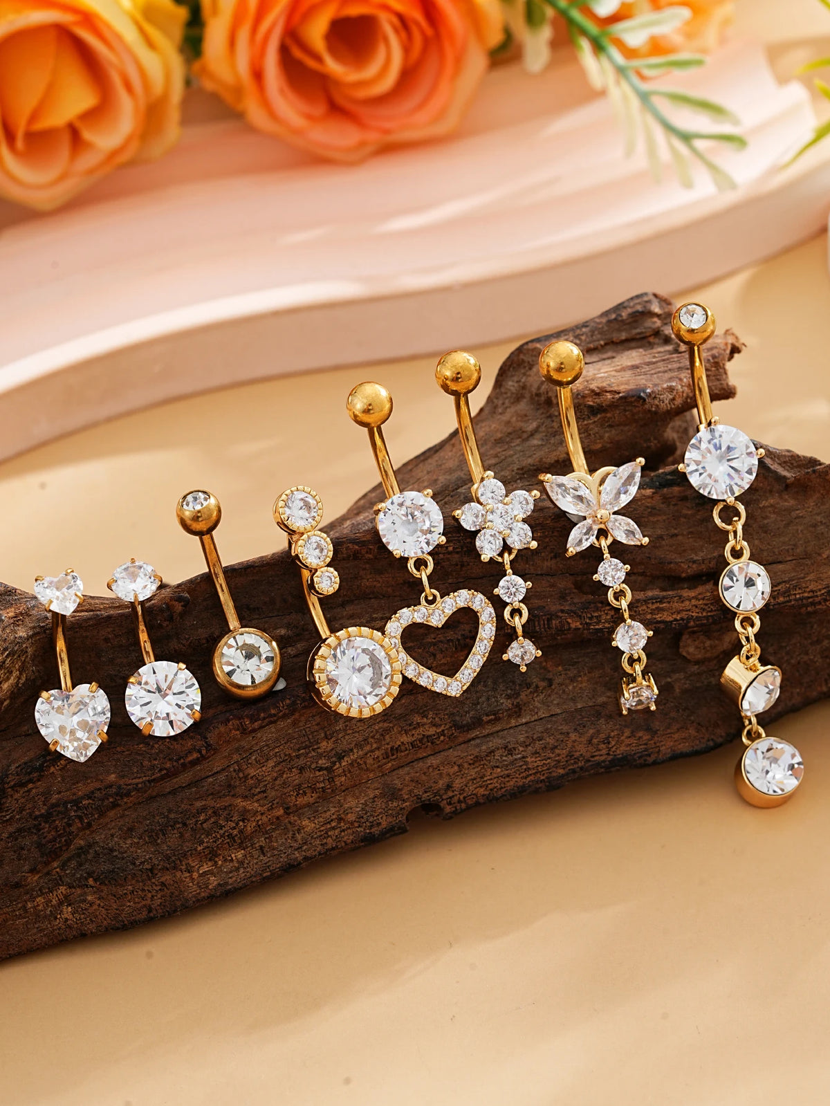 A set of gold dangle curved belly piercing jewelry featuring heart and flower designs on a wooden surface.