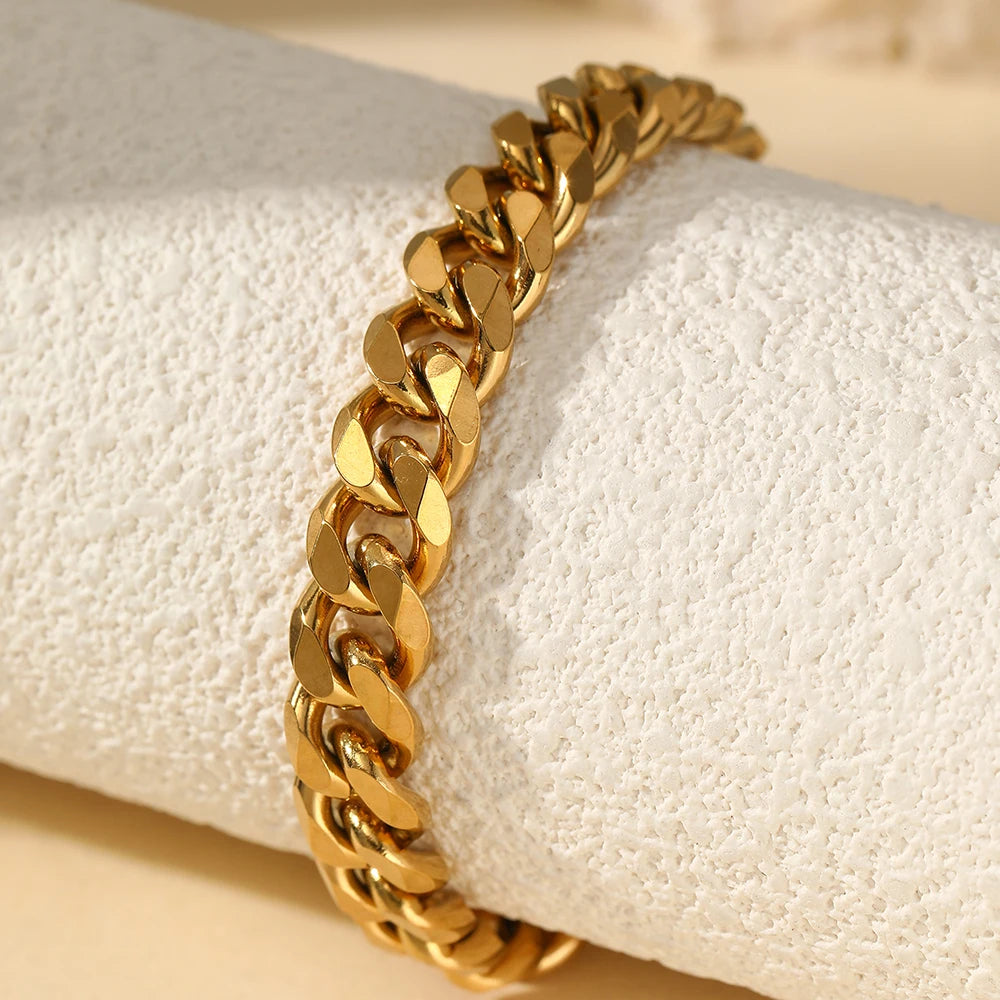 A gold-toned multi-chain stainless steel anklet worn on a wrist, resting on a white fabric background.