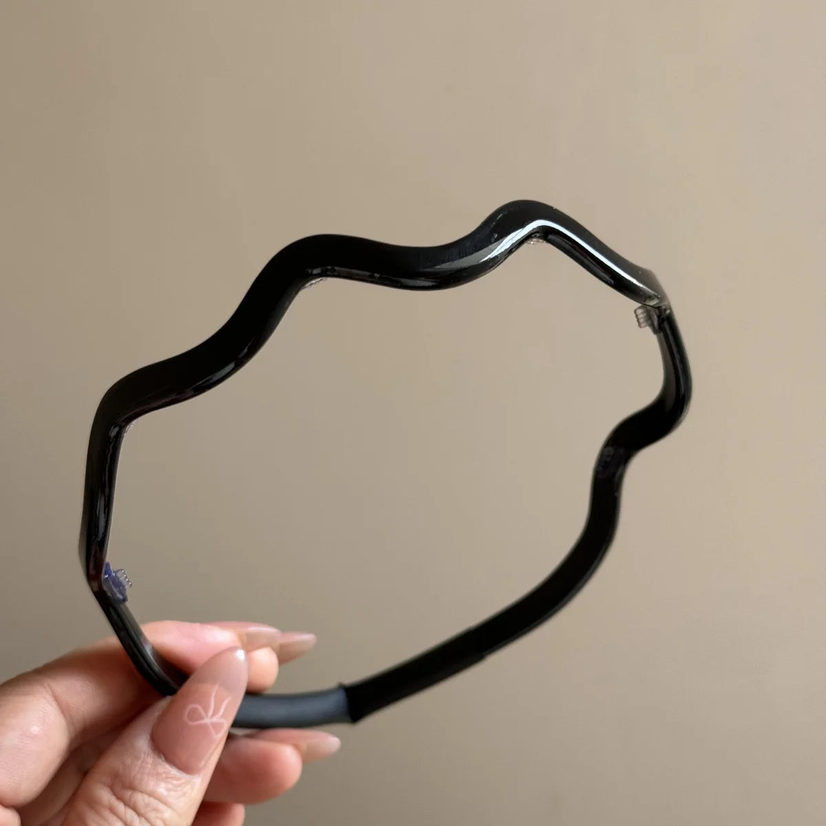 Una mano sostiene un aro de pelo de acetato negro y ondulado con un pequeño acento morado.