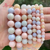 A hand holds a string of smooth round jade beads in various pastel shades of pink, white, and blue.