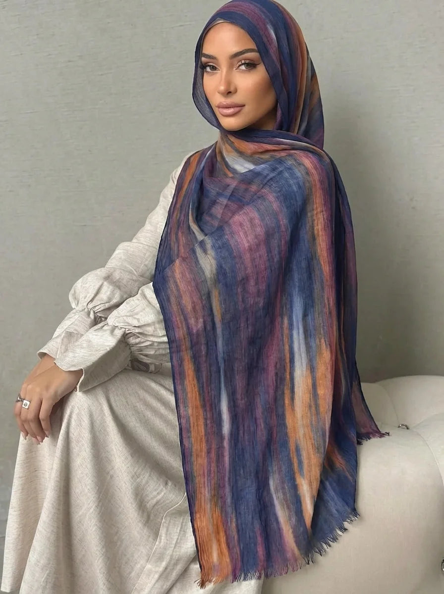 Una mujer vistiendo un elegante pañuelo de hijab a rayas morado y azul sobre una blusa beige clara.
