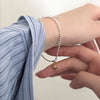 A hand is wearing a sterling silver double heart charm bracelet on a wrist, with a blue striped shirt visible.