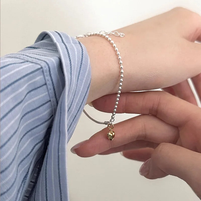 A hand is wearing a sterling silver double heart charm bracelet on a wrist, with a blue striped shirt visible.
