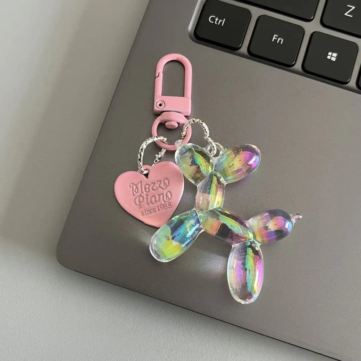 A pink and iridescent resin animal dog keychain hanging from a metal clasp on a silver laptop.