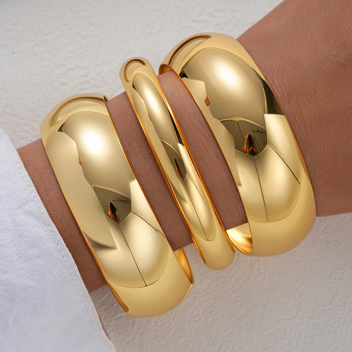 A set of three gold geometric wave bangles worn on a person's wrist.