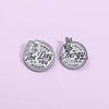 A silver enamel lapel brooch featuring a skull and hand design with the text Have The Day You Deserve and Match Energy So How