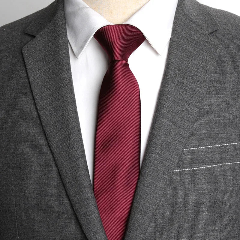 A close-up of a man wearing a dark gray suit jacket, white shirt, and a maroon patterned business tie.
