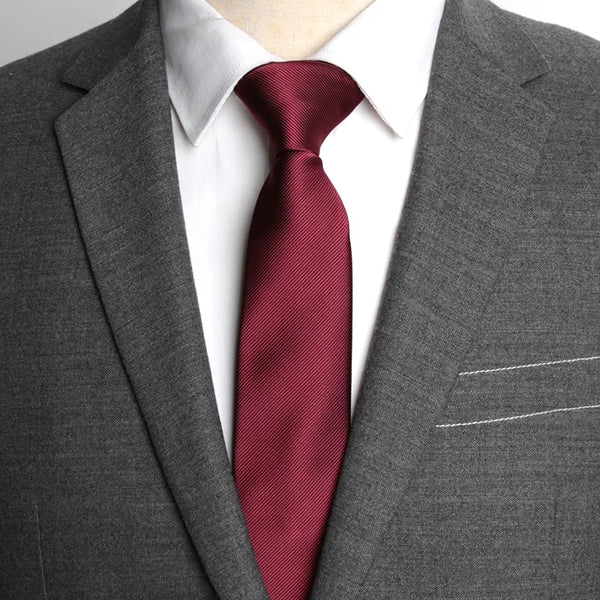 A close-up of a man wearing a dark gray suit jacket, white shirt, and a maroon patterned business tie.