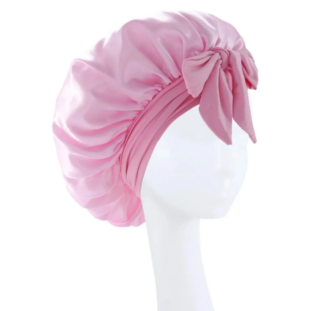 A pink satin wide-brimmed hair wrap headscarf tied in a bow displayed on a white mannequin.