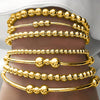 A set of gold-colored minimalist round beaded bracelets stacked on a person's wrist.