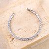 A silver bracelet set featuring a geometric design with clear rhinestones stacked together, displayed on a light beige surfac