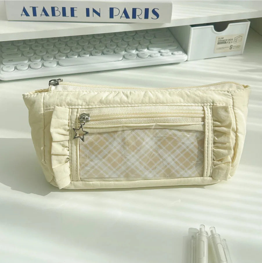 A cream-colored lace pencil case with a flap and decorative stitching is displayed on a white shelf.