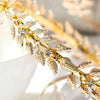 A close-up of a Greek gold leaf headband featuring delicate gold leaves and clear crystals.