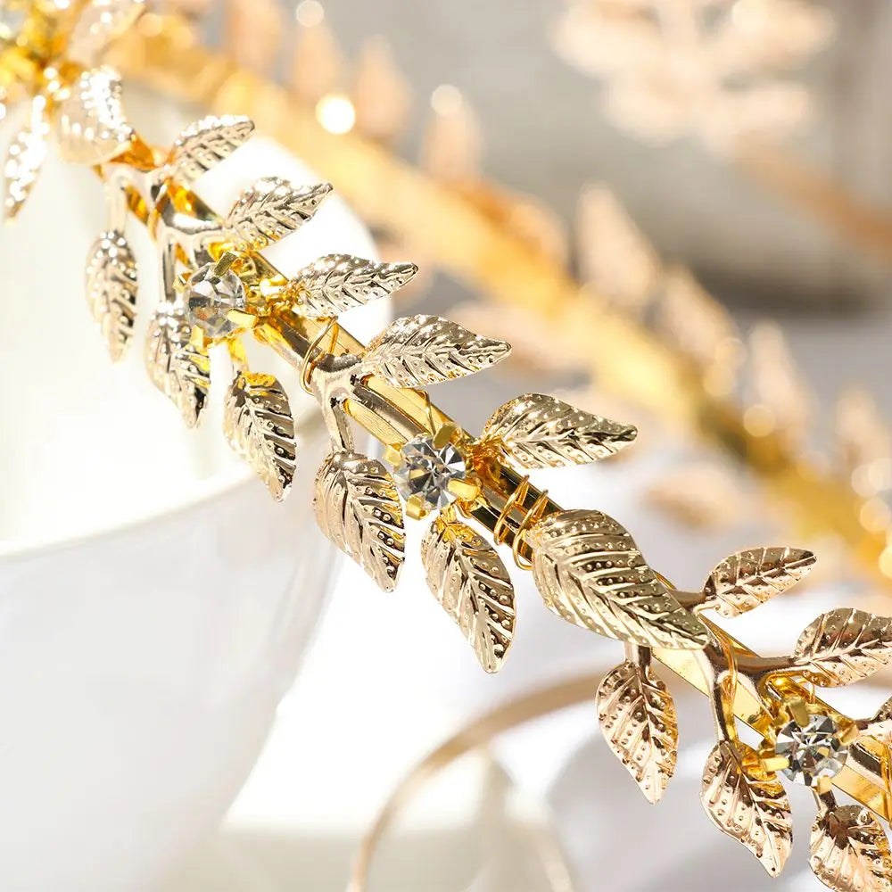 A close-up of a Greek gold leaf headband featuring delicate gold leaves and clear crystals.